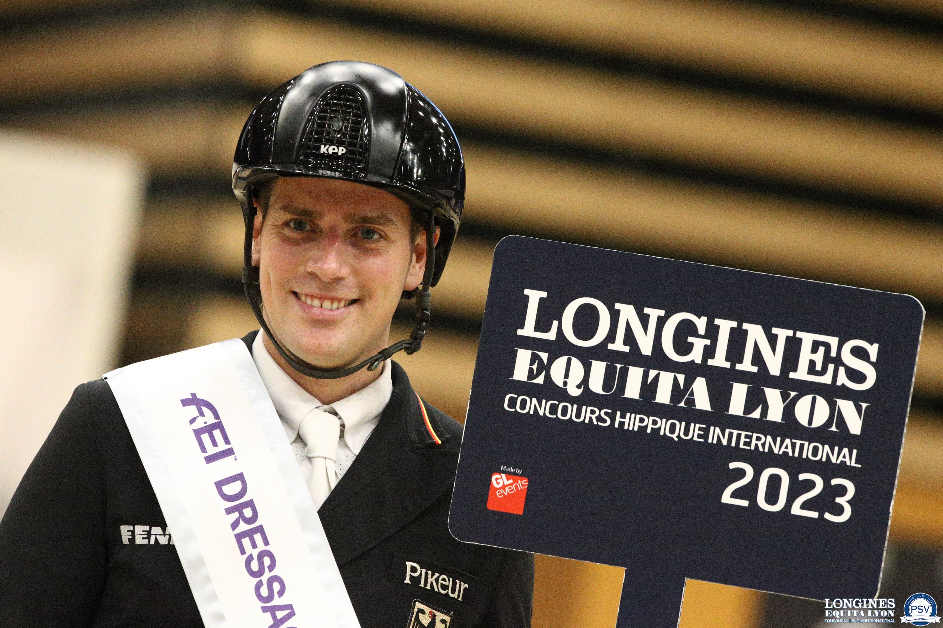 "Frederic Wandres souriant et tenant le panneau du Longines Equitalyon Concours Hippique International dans la main, suite à sa victoire"